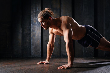 Obraz premium Young athletic guy in blue shorts on floor doing plank exercise on floor. Active strong fit sportsman do push-ups workout at gym with naked torso ripped shoulders. Sportive man, male, runner training