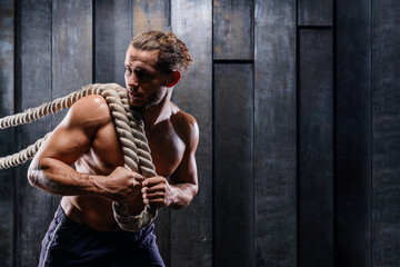 Fototapeta na wymiar Dynamic motion of sportive muscular man, athlete do exercise fitness with battle ropes. Male training upper body working out at hard cross-fit training. Brutal strong bodybuilder pumping up muscles.