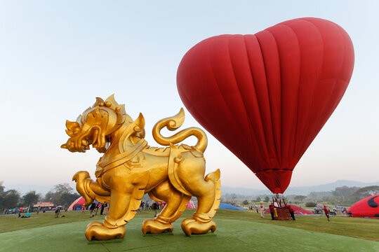 Chiang Mai Thai February 14 2019 a large golden Singha statue is installed on green hillside with red heart balloons rising in the background during Balloon Festival held in Singha Park, Chiang Rai.