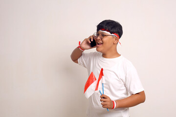 Happy asian boy standing while talking on phone and holding indonesian flag.Independence day concept