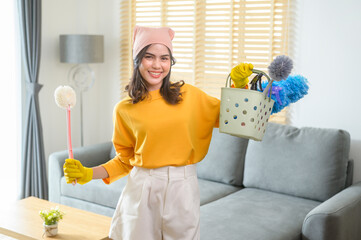 Young happy woman wearing yellow gloves  and holding a basket of cleaning supplies in living room.