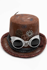 Studio photo of a steam punk hat. It is brown with goggles attached to them.