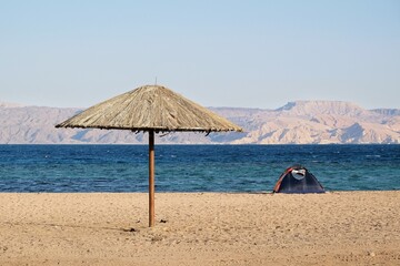Single tent and straw umbrella on beach by Red Sea around Aqaba, Jordan