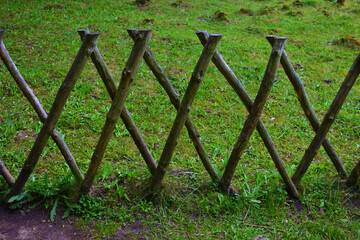 Fence made of crossed sticks on the background of a green lawn in a summer day. Natural forest background. Wildlife. Poland, park in the Kurnik castle, Poznan, June 2022.  © B.inna