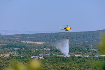 A yellow firefighting helicopter putting out a fire by dropping water. © Pablo