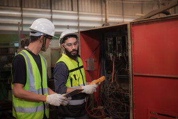 Electrician latin mixed-race and asian engineer in safety uniforms workwear Inspecting and maintaining the machine's electrical control cabinet in heavy industrial manufacturer factory.
