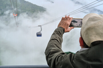 Close-up of man taking a photo on his smartphone from cable car cabin in the mountains. Traveling concept. 