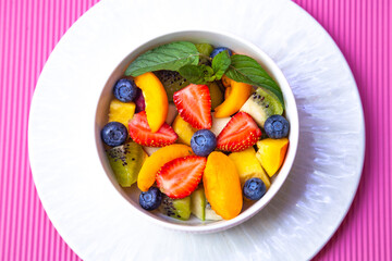 
Fruit salad with wooden honey spoon on pink background