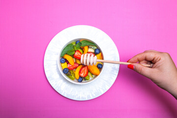
Fruit salad with wooden honey spoon on pink background