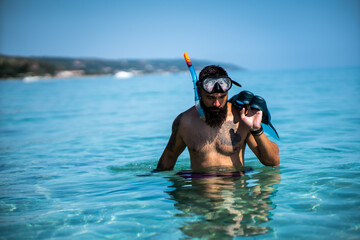 Young Caucasian male after diving or preparing to dive, holding diving fins while wearing goggles and breathing tube for diving.