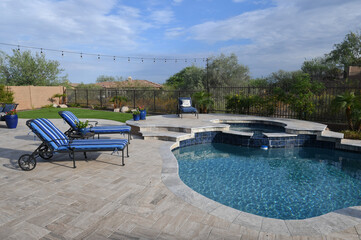 A desert landscaped backyard in Arizona featuring a travertine tiled pool deck.
