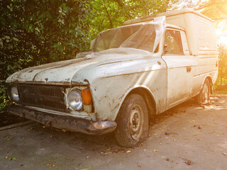 Obsolete dirty car with flat tires on the street. A dirty white cargo-passenger passenger car of an outdated model with flat wheels stands in the yard covered with polyethylene