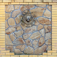 Iron head of a lion on a stone wall. Stone fence with forged gilded lion's head