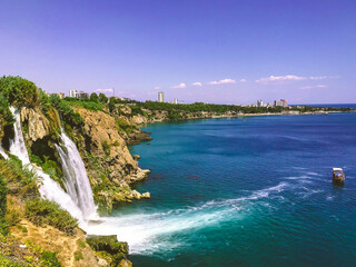 Fototapeta premium sea waterfall. a large boat with tourists floats in the sea. white foam of sea water. stone mountain with green mountains and plants