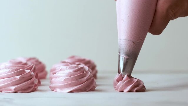 Squeezing whipped pink cream with pastry bag  for raspberry marshmallow. Close up of confectioner making marshmallow on the white background