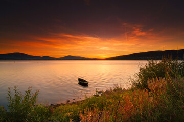 Samotna łódka unosi się na jeziorze podczas zachodu słońca