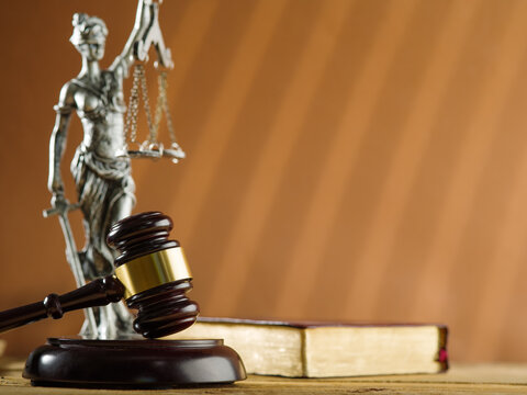 Symbols of a fair trial. On a beige background is a bronze figurine of the goddess of justice - Themis, a book and a wooden gavel of a judge. Rule of law, law, justice, constitution, bible.