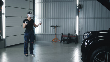 Woman asian mechanic in uniform and in modern virtual reality headset with controllers moving her hands, while checking a car with a breakdown in car service