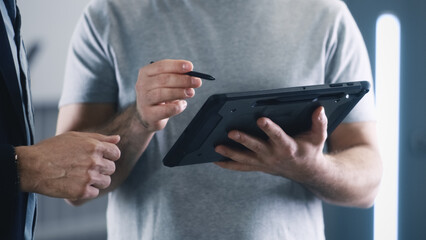 Crop mechanic in t-shirt consulting a client in a car service using tablet and discussing the results of a car checking and diagnostics