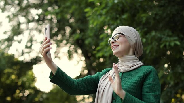 Smiling happy beautiful muslim woman relaxing using digital smartphone. Young muslim girl looking at screen speaking during online video call on social media on city.
