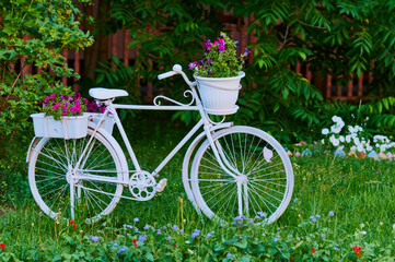 Fototapeta na wymiar A white bicycle adorns a section of the park. Landscaping. Decorative flowers, grass and bushes. Selective focus.