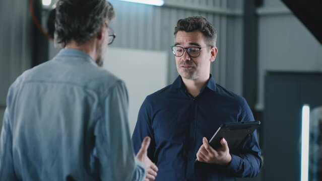 Cheerful car service manager in repair shop with tablet and client shaking hands after successfully diagnosing and repairing car