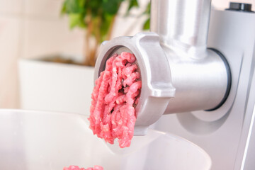 A man processes meat in an electric meat grinder. Preparation of minced beef and pork for cutlets,...