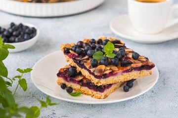 Sliced oatmeal cake with blueberries and almonds on a white plate on a light concrete background. Baking with berries.