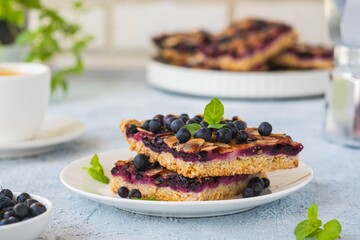 Sliced oatmeal cake with blueberries and almonds on a white plate on a light concrete background. Baking with berries.