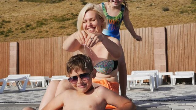 caucasoid mom and two teenage children have fun swimming and splashing in the water in the pool. A boy sitting in a bathing circle floats on the water, mother and sister pour water over