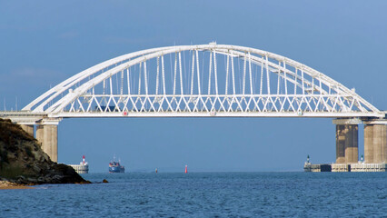 Obraz premium Breathtaking seascape with a white beautiful bridge with many moving cars above the water surface and sailing ships, time lapse effect. Shot. Calm sea with ripples, huge bridge, vessel and bue sky.