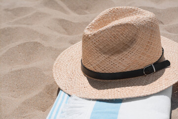 Fototapeta na wymiar Straw hat and beach towel on sand, closeup. Space for text