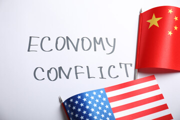 USA and China flags near words ECONOMY CONFLICT on white background, flat lay