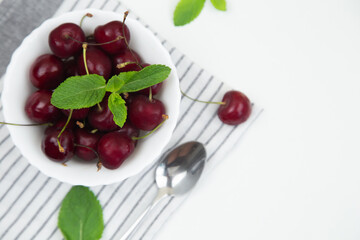 A white plate with a ripe burgundy cherry and a mint petal stands on a striped kitchen towel on a white background, top view. High quality photo