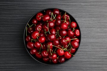 Bowl with ripe sweet cherries on dark wooden table, top view