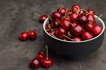 Bowl with ripe sweet cherries on dark grey table, space for text