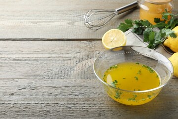 Bowl with lemon sauce and ingredients on wooden table, space for text. Delicious salad dressing