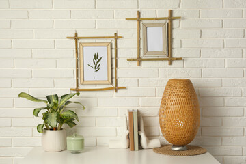Potted houseplant, decor elements and books on white table near brick wall with stylish bamboo...