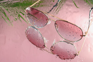 Stylish sunglasses with water drops on glass table, closeup