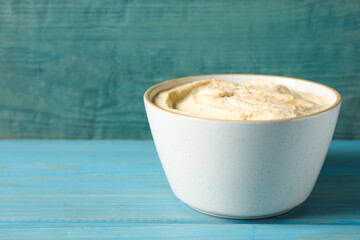 Tasty hummus in bowl on light blue table against wooden background. Space for text