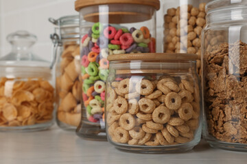 Glass containers with different breakfast cereals on white countertop, closeup