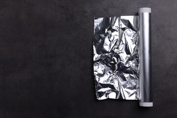 Roll of aluminum foil on dark grey table, top view. Space for text