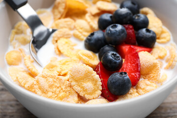 Bowl of tasty crispy corn flakes with milk and berries on wooden table, closeup