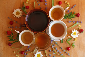Cups with tasty herbal tea, different flowers and fruits on wooden table, flat lay