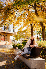 a beautiful blonde in a coat and jeans on the bench in an autumn park. 