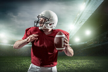 American football sportsman player with ball in action on stadium under lights of background. Sport, proud footballer in white helmet and red t-shirt ready to play.
