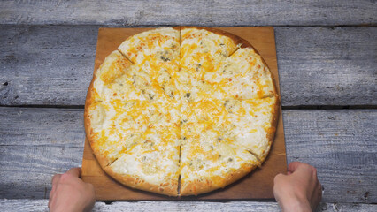 Hot four cheeses delicious pizza lying on a tray on wood grey boards background. Frame. Close up for hands putting a board with a pizza circle on wood surface. - Powered by Adobe