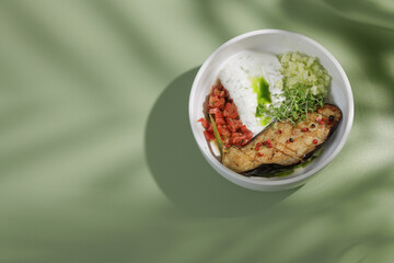 baked eggplant with white sauce and lettuce on green background with shadow from palm tree, top view