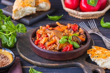 Ajapsandali, cold vegetable stew or appetizer of eggplant, pepper, tomato and carrots in a clay bowl on a brown wooden background. eggplant recipes.