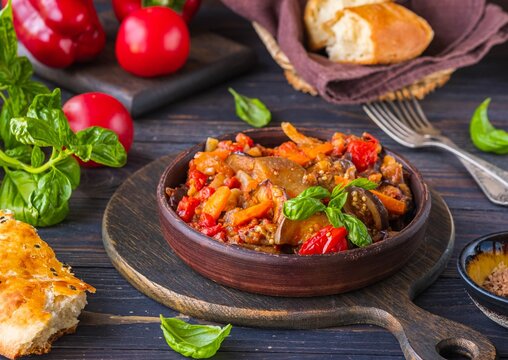 Ajapsandali, cold vegetable stew or appetizer of eggplant, pepper, tomato and carrots in a clay bowl on a brown wooden background. eggplant recipes.